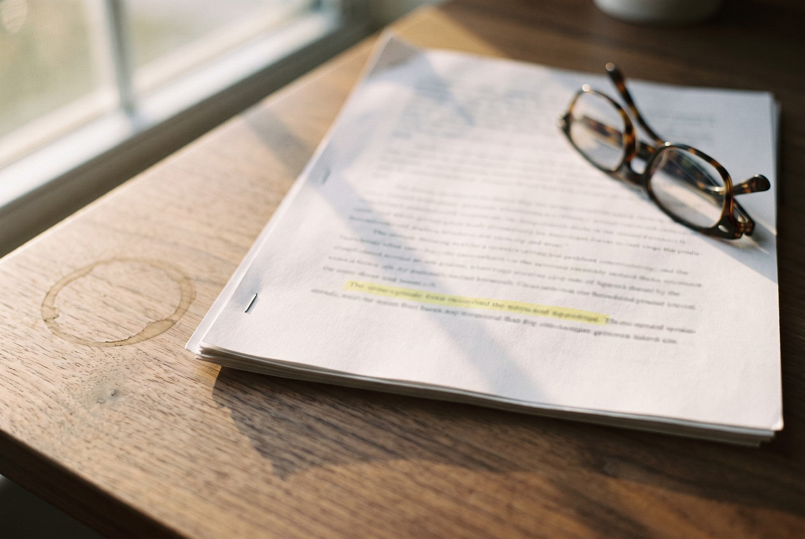 A printed research paper on a desk with one line highlighted and reading glasses resting on top