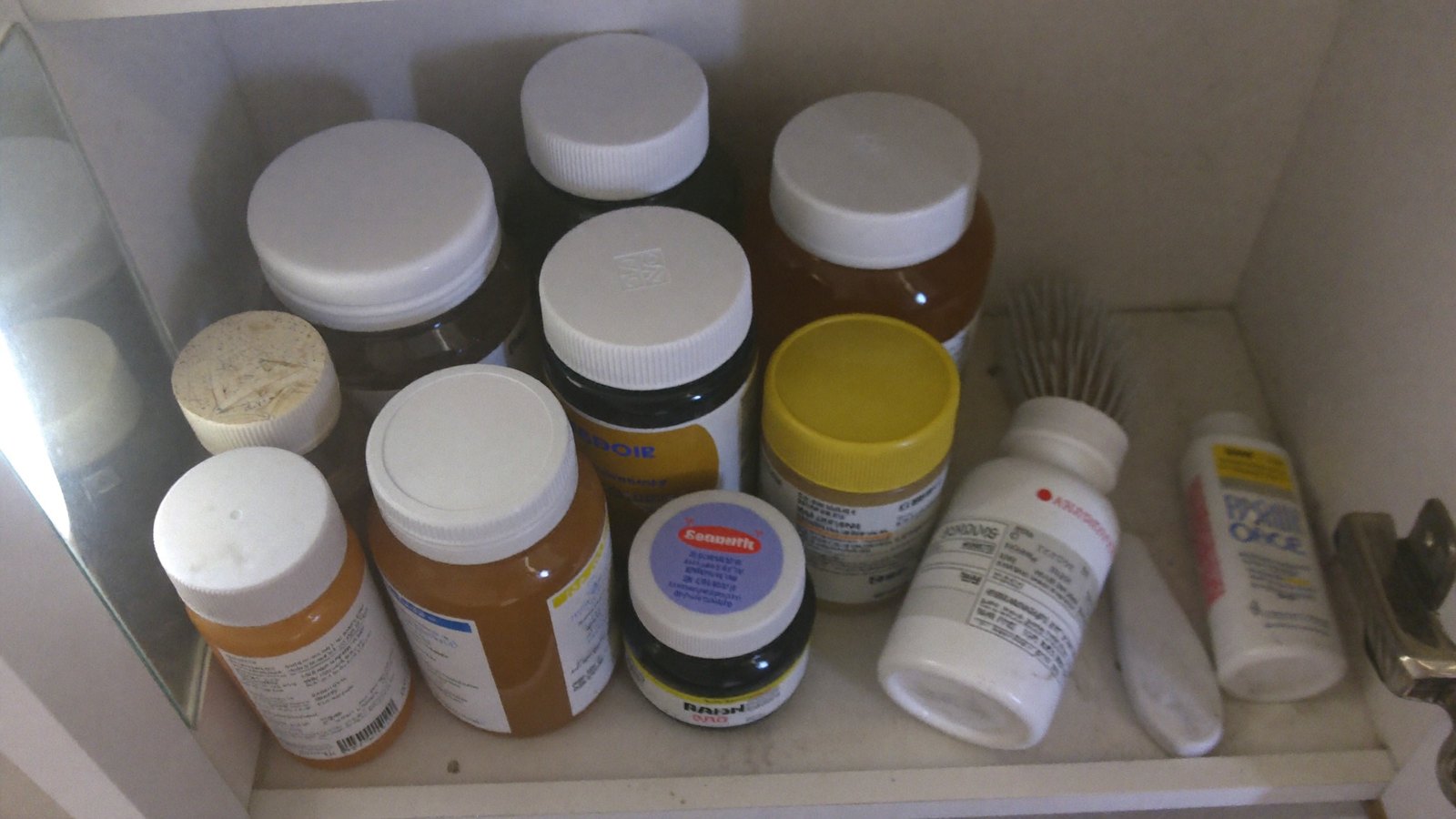 A bathroom cabinet shelf crowded with part-used supplement bottles